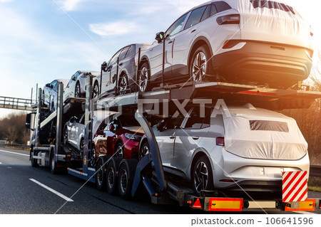 Tow truck car carrier semi trailer on highway carrying batch of new wrapped electric SUVs on motorway road at sunset evening time. Business distribution logistics service. Lorry driving highway Tow truck car carrier semi trailer on highway carrying batch of new wrapped electric SUVs on motorway road at sunset evening time. Business distribution logistics service. Lorry driving highway 106641596