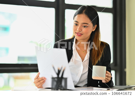 Attractive female manager reading paper document, statistics, financial results at office desk Attractive female manager reading paper document, statistics, financial results at office desk 106641672