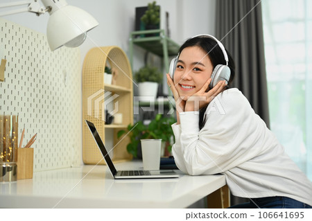 Pretty young asian woman wearing headphone learning distantly, attending virtual class via laptop 106641695