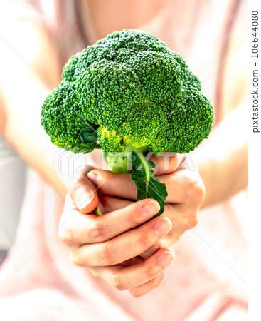 The lady is holding fresh green broccoli and giving it to the camera. 106644080