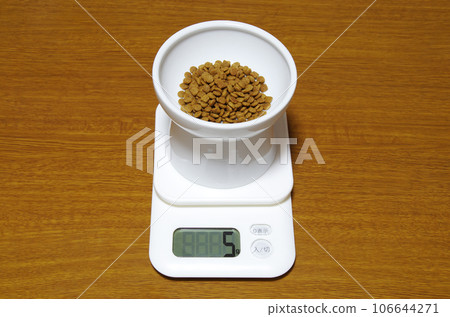A container of cat food is placed on a digital scale that shows 5g. A container of cat food is placed on a digital scale that shows 5g. 106644271