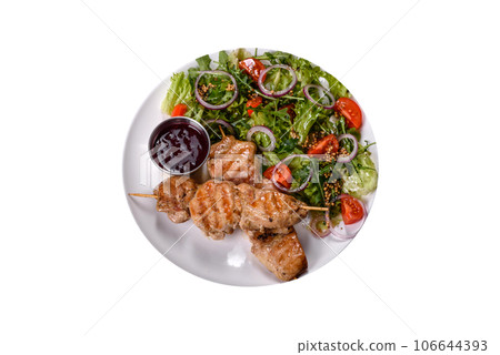 Pieces of chicken fillet baked on grilled wooden sticks with salad and red sauce 106644393