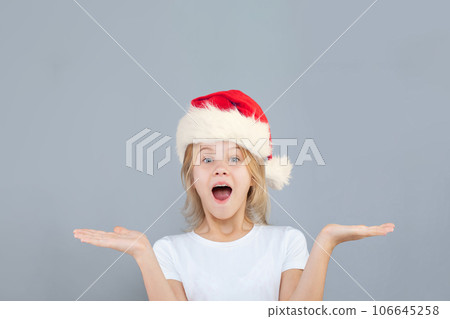 Christmas teen girl in Santa hat with empty open palm hands on blue banner background Christmas teen girl in Santa hat with empty open palm hands on blue banner background 106645258