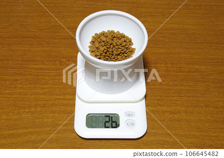 A container of cat food is placed on a digital scale that shows 26g. A container of cat food is placed on a digital scale that shows 26g. 106645482