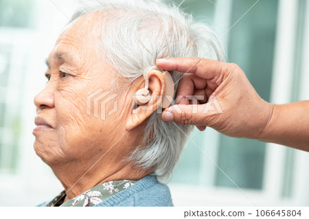 Asian senior woman patient wearing a hearing aid for treating hearing loss problem. Asian senior woman patient wearing a hearing aid for treating hearing loss problem. 106645804