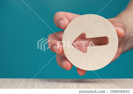 Arrow pointing left on a blue background. Banner with an arrow in a wooden circle in a hand close-up points to the left with copy space. 106646642