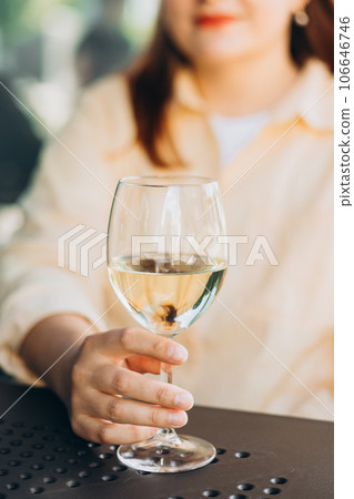 White wine glass in an outdoor cafe. Happy 30s woman sitting on the cafe terrace on the city street. Traveler. Woman hands toasting with wine 106646746