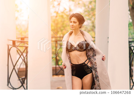 Young beautiful dark-haired woman with slender figure in lingerie and classic coat in autumn park 106647268