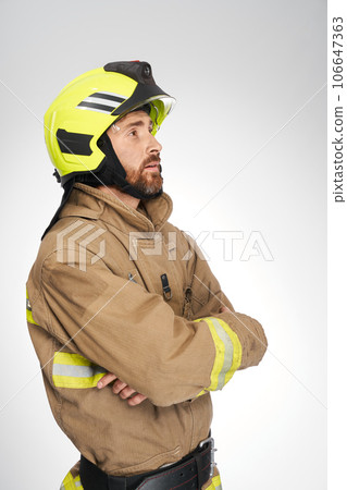 Strong, serious guy in fireman's uniform looking up and away in studio. Side view of firefighter waiting, with crossed hands, isolated on white background. Concept of work, firefighting, hope. Strong, serious guy in fireman's uniform looking up and away in studio. Side view of firefighter waiting, with crossed hands, isolated on white background. Concept of work, firefighting, hope. 106647363