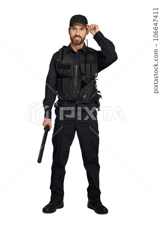 Handsome cop in uniform adjusting police cap, while standing in studio. Front view of bearded officer with truncheon, wearing black peaked cap, isolated on white background. Uniform, outfit concept. Handsome cop in uniform adjusting police cap, while standing in studio. Front view of bearded officer with truncheon, wearing black peaked cap, isolated on white background. Uniform, outfit concept. 106647411