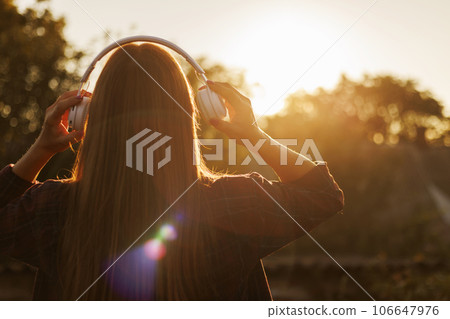 Young woman in headphones listening to music at sunset 106647976