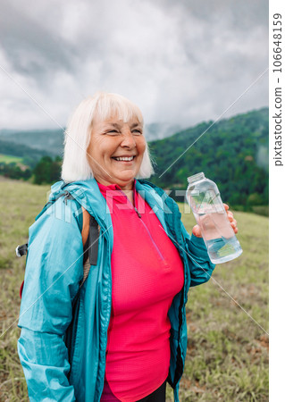 caucasian 50s blonde girl drinking water from plastic bottle. Mountain background  106648159