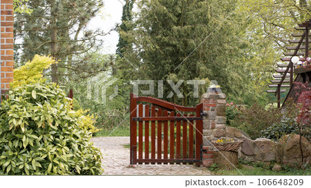 Beautiful brown wooden gates in a green garden, one part slightly open, inviting you inside 106648209