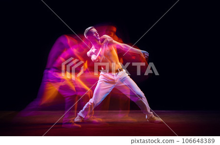 Inspiration and freedom. Young shirtless guy making chaotic movements against black studio background in neon with mixed lights effect 106648389
