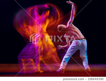 Inspiration and freedom. Young shirtless guy making chaotic movements against black studio background in neon with mixed lights effect 106648390