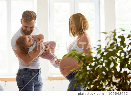 Young man and woman, parent playing with little daughter at home. Woman expecting second baby Young man and woman, parent playing with little daughter at home. Woman expecting second baby 106648432