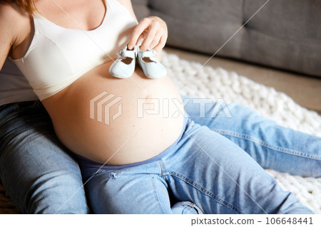 Care, love and support. Cropped image of pregnant female belly with little shoes on it. Parents expecting baby Care, love and support. Cropped image of pregnant female belly with little shoes on it. Parents expecting baby 106648441