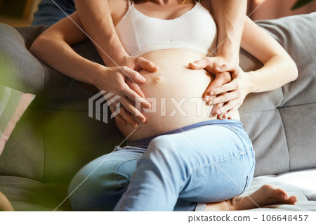 Cropped image of male and female hands on pregnant woman's belly. Young couple expecting baby Cropped image of male and female hands on pregnant woman's belly. Young couple expecting baby 106648457