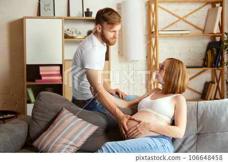 Support and care. Loving man, husband holding hand on his wife belly. Couple spending time at home together 106648458