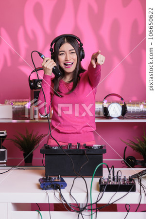 Asian artist performing electronic music using professional turntables, enjoying to perform in club at night. Smiling performer mixing techno sound, talking into microphone with fans Asian artist performing electronic music using professional turntables, enjoying to perform in club at night. Smiling performer mixing techno sound, talking into microphone with fans 106650622