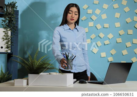 Sad female employee after being fired by boss picking up personal belongings from workstation in startup company. Business woman quitting her job due to professionals problems. Sad female employee after being fired by boss picking up personal belongings from workstation in startup company. Business woman quitting her job due to professionals problems. 106650631