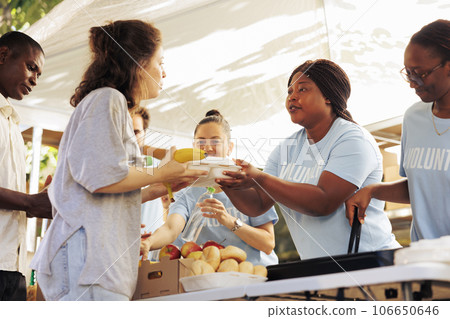 Multiracial volunteers handing out meal donations to the needy at a food drive. Image showing voluntary people generously supporting the homeless and those experiencing poverty and hunger. Multiracial volunteers handing out meal donations to the needy at a food drive. Image showing voluntary people generously supporting the homeless and those experiencing poverty and hunger. 106650646