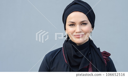 Muslim woman in black hijab smiling against grey wall Muslim woman in black hijab smiling against grey wall 106652516