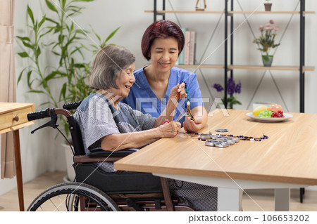 Caregiver and senior woman playing stringing beads for dementia prevention 106653202