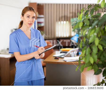 Young woman therapist writes notes on a tablet, standing in a office Young woman therapist writes notes on a tablet, standing in a office 106653600
