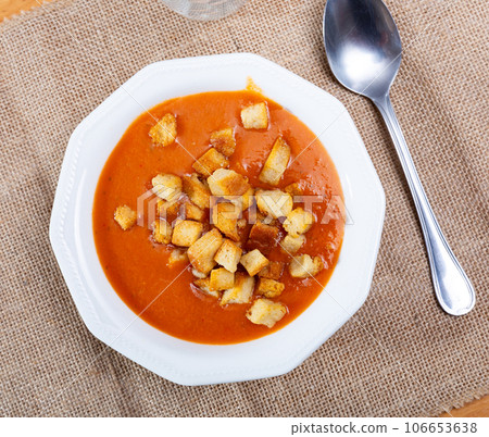 There is plate with cream carrot soup of orange color on table, decorated with small toasted crouton There is plate with cream carrot soup of orange color on table, decorated with small toasted crouton 106653638