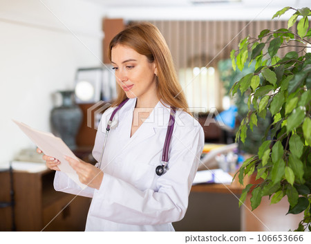 Doctor woman standing in hall with sheets of paper in hands Doctor woman standing in hall with sheets of paper in hands 106653666