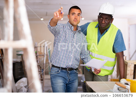 Owner of apartment indicates to worker in yellow vest where to start repairing room Owner of apartment indicates to worker in yellow vest where to start repairing room 106653679