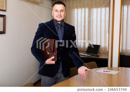 Man in suit with briefcase in hand standing in office Man in suit with briefcase in hand standing in office 106653740