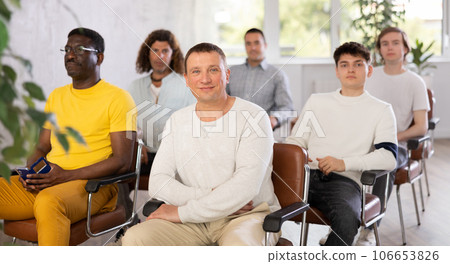 Smiling middle-aged man sitting in auditorium together with a group of guys 106653826