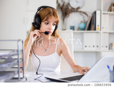 Office worker woman is working at a computer and talking by headset with client in office Office worker woman is working at a computer and talking by headset with client in office 106653956