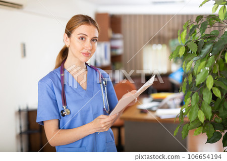 Young female therapist is studying important documents while standing in the office Young female therapist is studying important documents while standing in the office 106654194