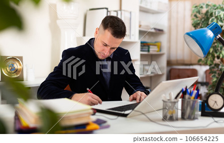 Positive businessman working with laptop and documents in office Positive businessman working with laptop and documents in office 106654225