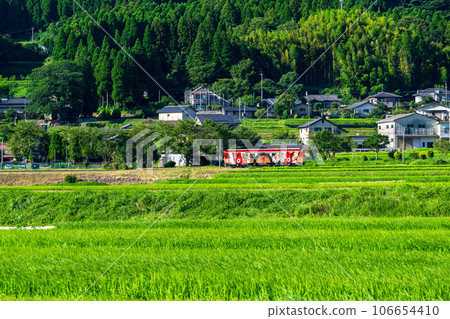 Rural scenery around the station building with the Aso mountain range in the background and the Sunny train [Aso Shimoda Castle Fureai Onsen Station] "Minami Aso Railway, all lines open" 106654410