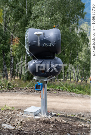 Yellow snow cannon on the edge of a hill overlooking a valley in summer or warm winter, green mountain peaks. Ski slope without snow in summer or during warm winter, greenhouse effect concept. Yellow snow cannon on the edge of a hill overlooking a valley in summer or warm winter, green mountain peaks. Ski slope without snow in summer or during warm winter, greenhouse effect concept. 106655750