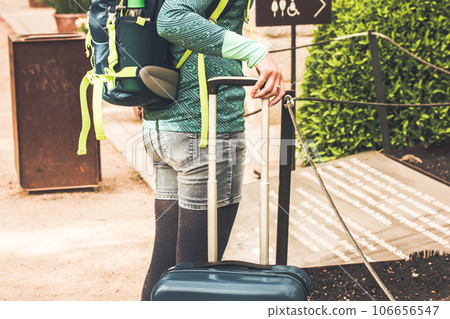 A woman tourist standing on a city street with a suitcase. Traveling solo in summer sunny day. Moving around a world. People with garbage at train station waiting for train. Faceless person traveling. 106656547