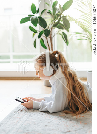 Little girl listening music lying on the floor Little girl listening music lying on the floor 106656874