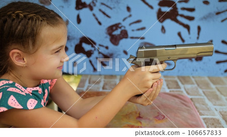 Little girl shoots at shooting range with gun. Outdoors entertainment for tourists in Thailand. Active leisure on vacation, traveling in Asia. Practice in shooting gallery safe legal pistol weapons. 106657833