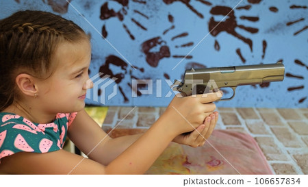 Little girl shoots at shooting range with gun. Outdoors entertainment for tourists in Thailand. Active leisure on vacation, traveling in Asia. Practice in shooting gallery safe legal pistol weapons. 106657834