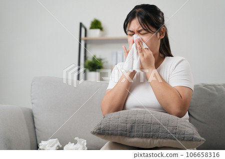 Young woman got a nose allergy sneezing sitting on the sofa at home.  Flu, Influenza, Sick, Fever, Illness. Healthcare and medical concept. 106658316