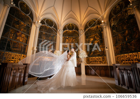 Bride and groom taking wedding photos at church with veil floating Bride and groom taking wedding photos at church with veil floating 106659536
