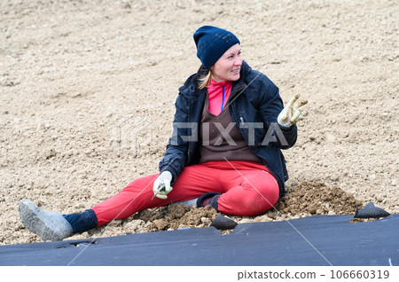 A woman sits on the ground, works in the field, the ground is covered with agrofibre. A woman sits on the ground, works in the field, the ground is covered with agrofibre. 106660319