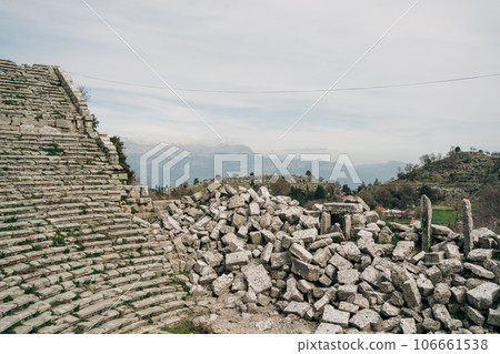 Scenic view of ancient antique ruins remnants of stone stadium arena coliseum amphitheater with rock boulder stone debris lying in the side under the cloudy sky 106661538