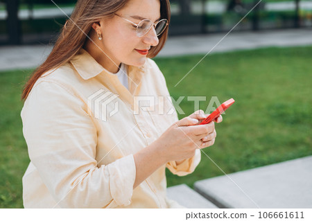 Smiling woman text messaging on smart phone at sunny day. Urban lifestyle concept. Traveler sitting n the bench and reading news on smartphone, fast connection, checking mobile apps outdoors. 106661611