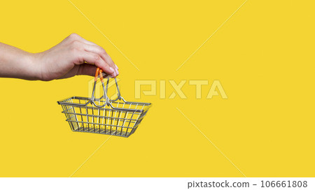 Female hand holds toy metal shopping basket on yellow background. Female hand holds toy metal shopping basket on yellow background. 106661808