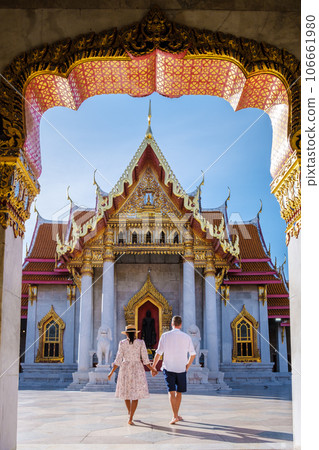 Asian woman with a hat and European men visiting a temple, a couple on a city trip in Bangkok Thailand, Wat Benchamabophit temple in Bangkok Thailand, The Marble temple in Bangkok.  106661980